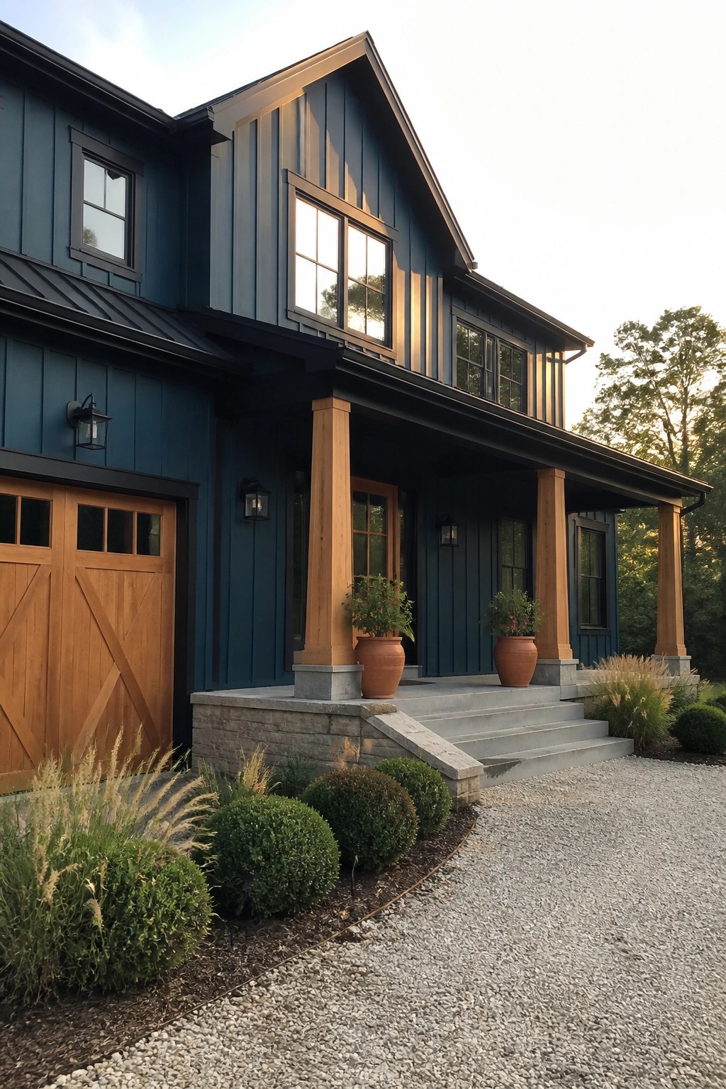 A two-story house with dark teal vertical siding, matte black window frames and trim, a wooden garage door, and a covered porch supported by wooden columns on stone bases.