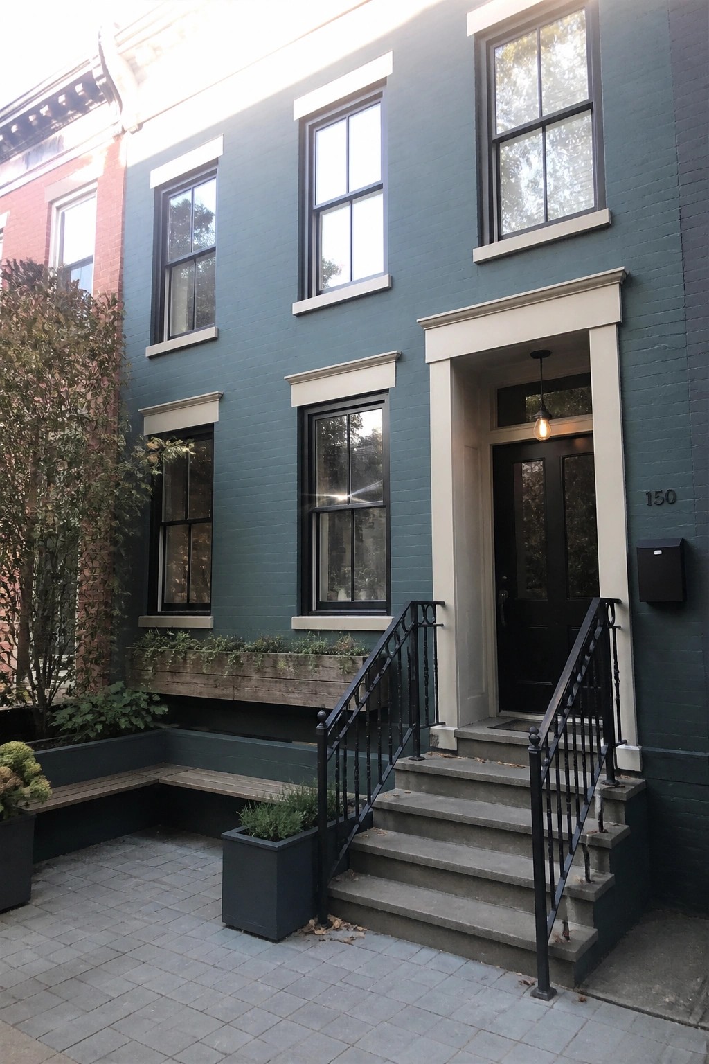 A dark teal brick house with matte black windows, a black front door, light trim, and concrete steps with black railings.