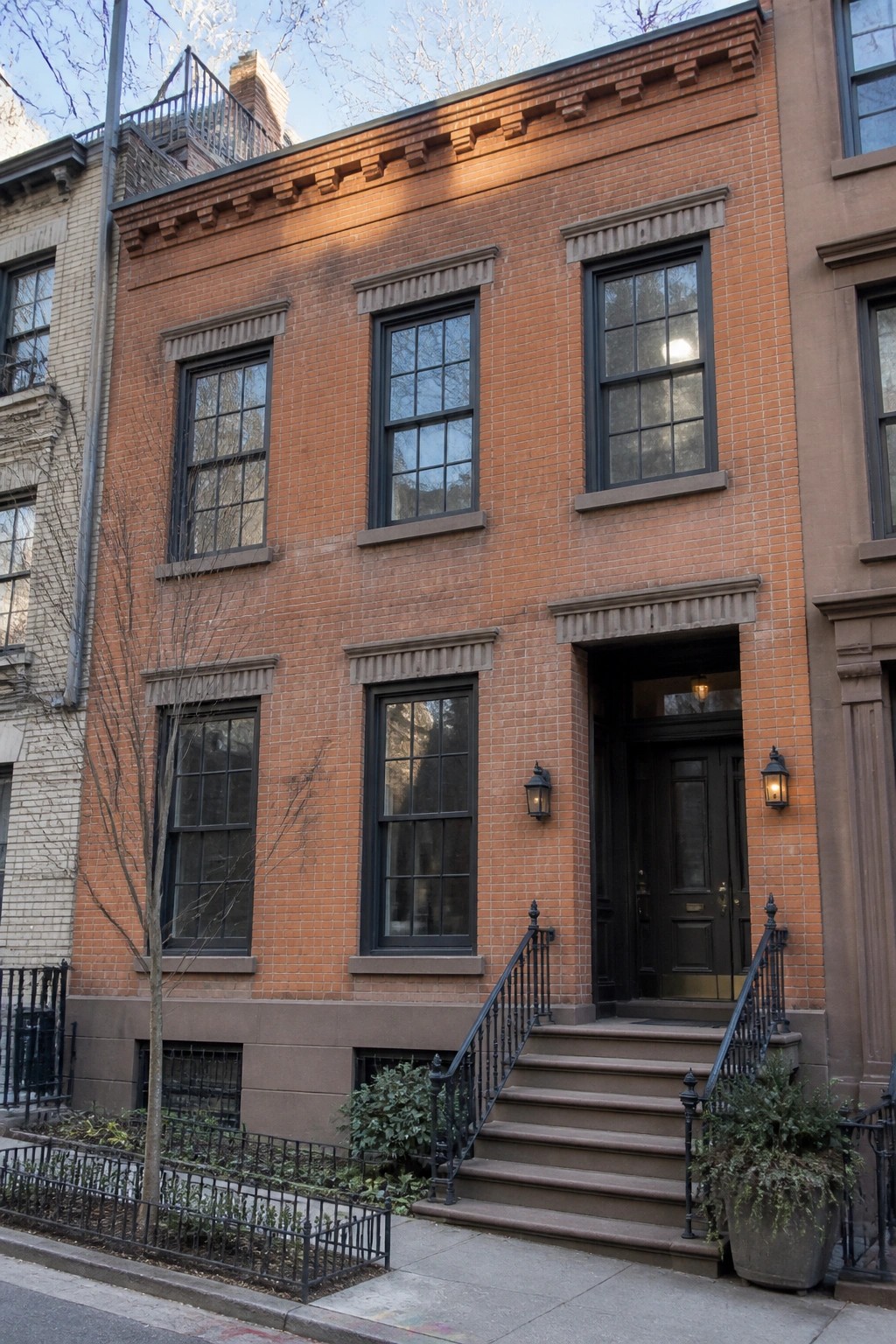 A two-story orange brick house with dark bronze window frames, a dark front door, and stone steps leading to the entrance.