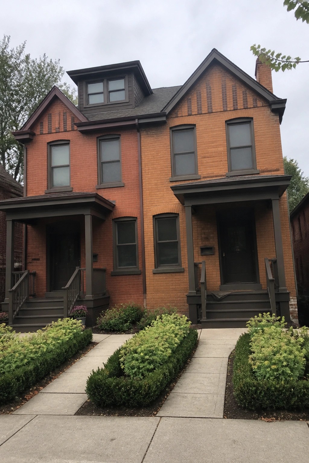 A two-story orange brick house with dark bronze windows, trim, and two matching front porches.