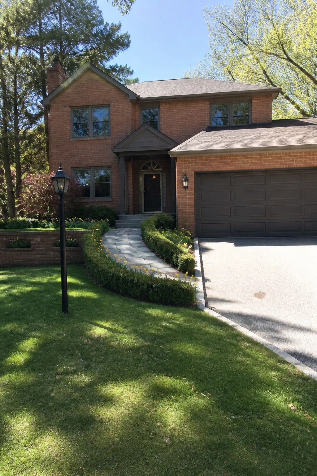 A two-story orange brick house with dark-framed windows, a dark garage door, and a curved stone walkway leading to the front door.