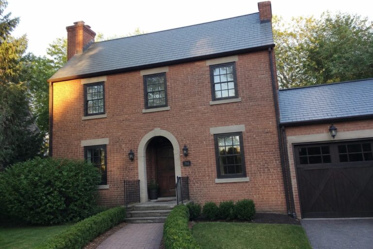 A two-story orange brick house with dark-framed windows, a dark wood garage door, and a curved stone entry with steps.