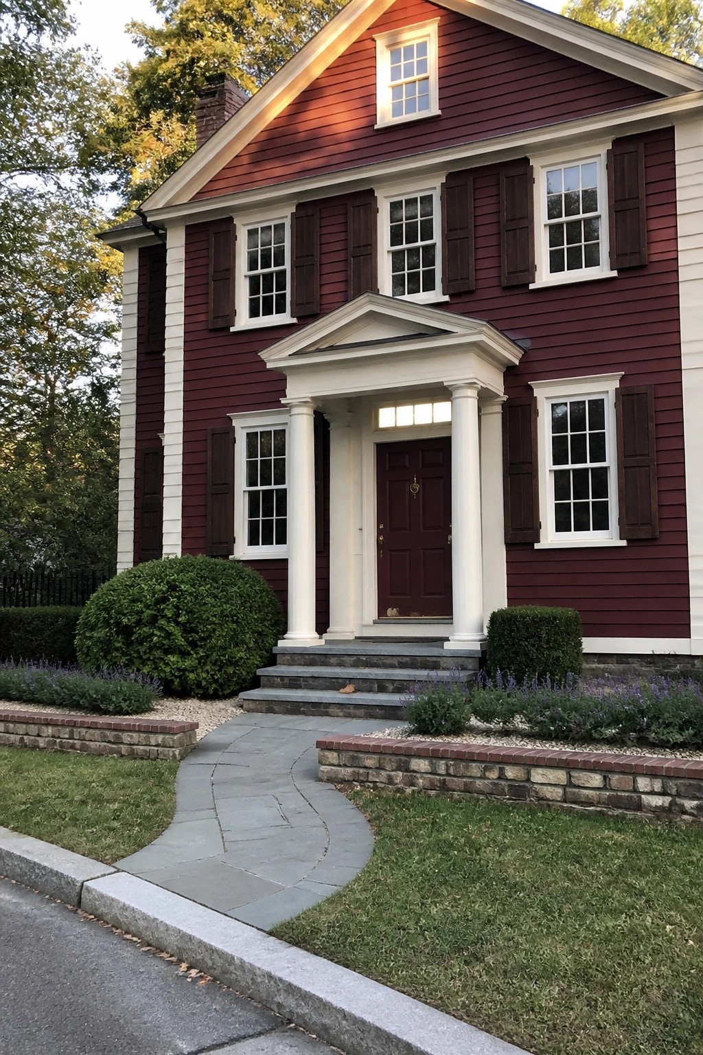 A two-story maroon house with white trim, dark shutters, and a white columned portico over the front door.