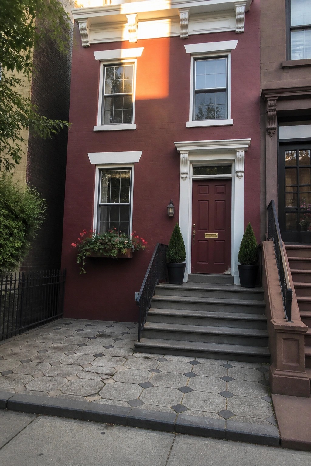 Red rowhouse with white trim, red door, stone steps, and potted plants.