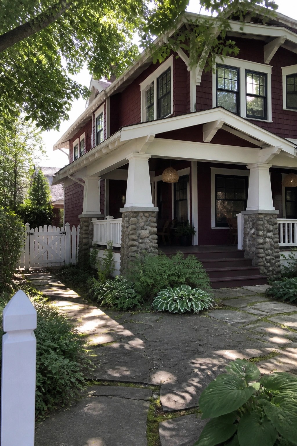 Red house with white porch on stone pillars and lush garden path