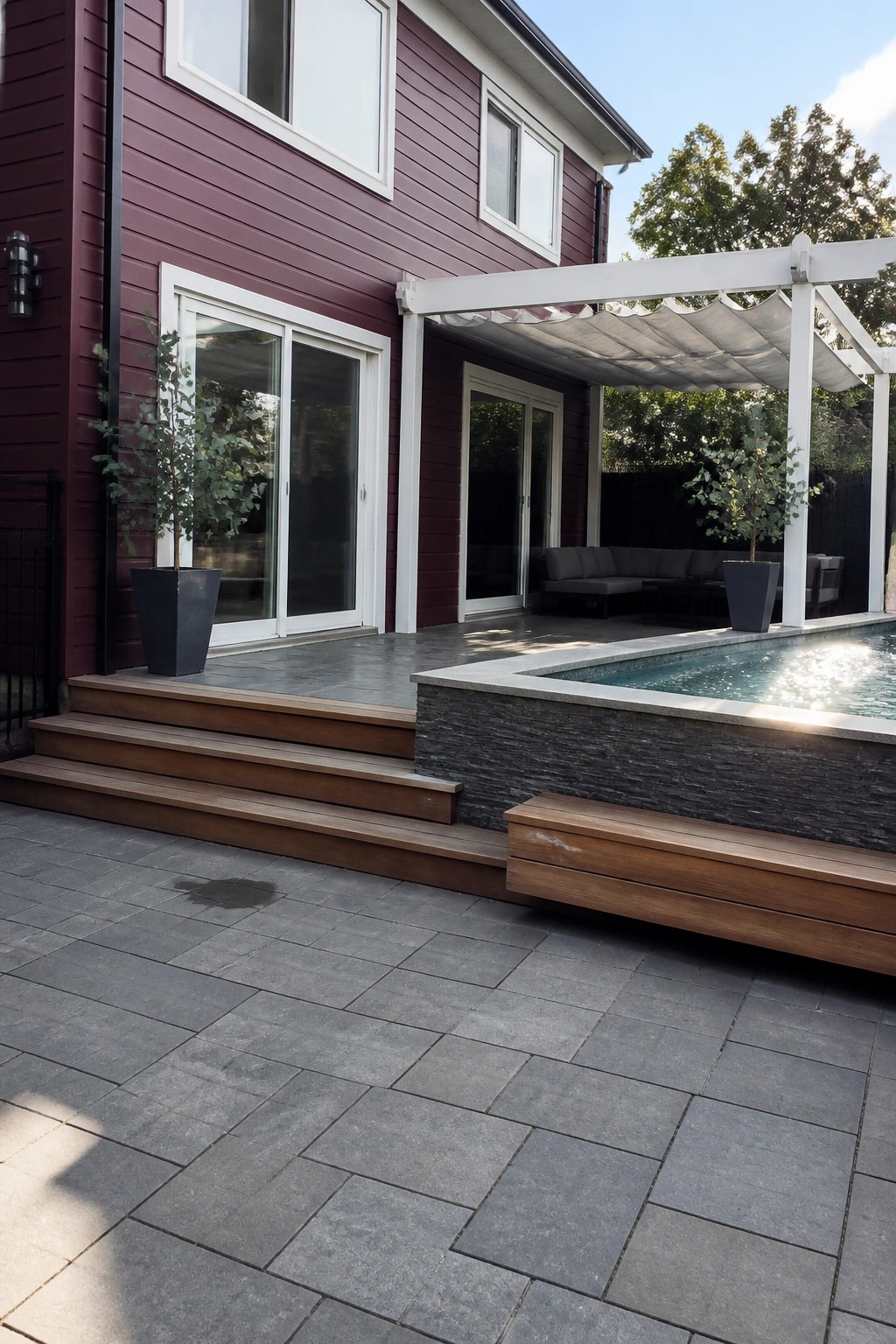 A two-story house with maroon siding and white trim, large glass doors, a white pergola over a patio, and a swimming pool with stone surround.