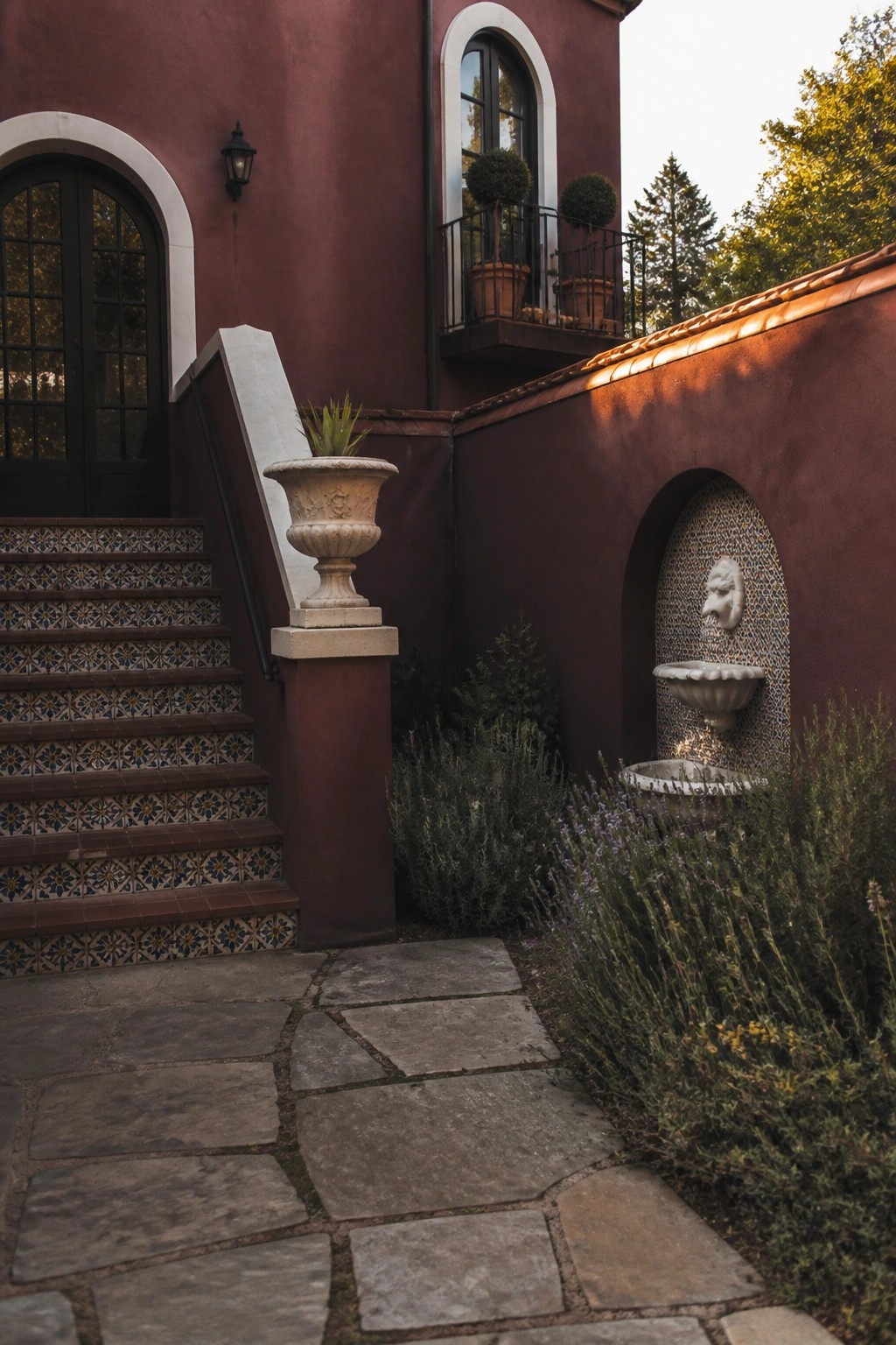 Red stucco building with tiled stairs, stone path, and wall fountain.