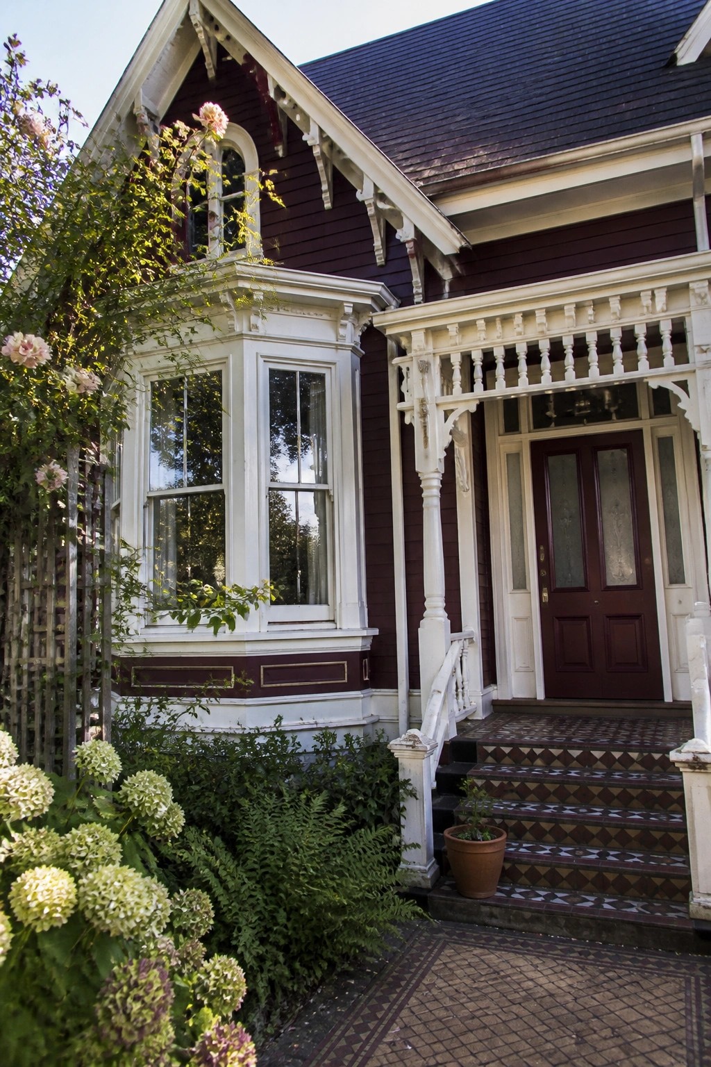 Victorian house with burgundy siding, ornate white trim, bay window, and blooming hydrangeas.