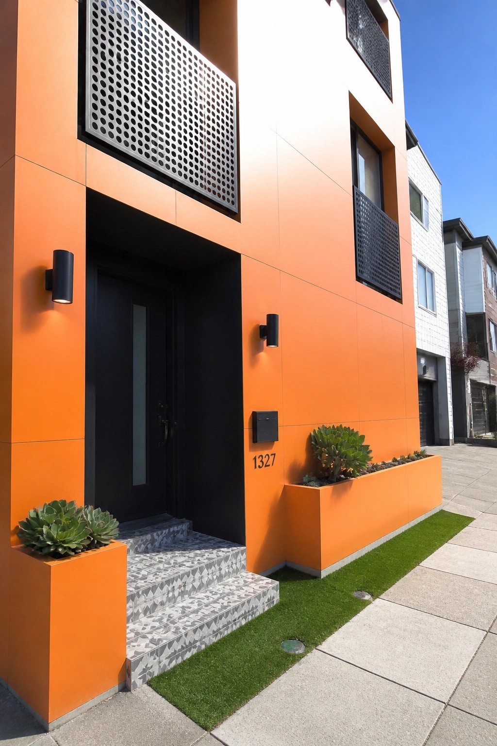 A modern two-story house with bright orange smooth fiber cement panels, a black front door, patterned tile steps, and a small orange planter box with succulents.
