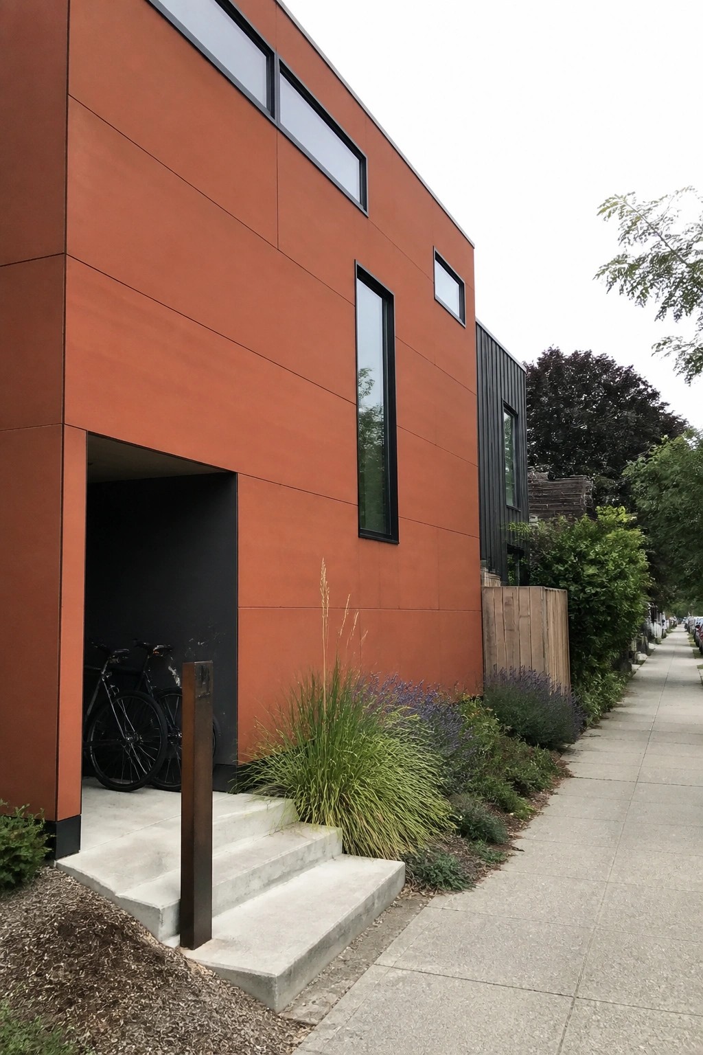 A modern two-story house clad in large smooth orange fiber cement panels with black window frames and a recessed dark entry.