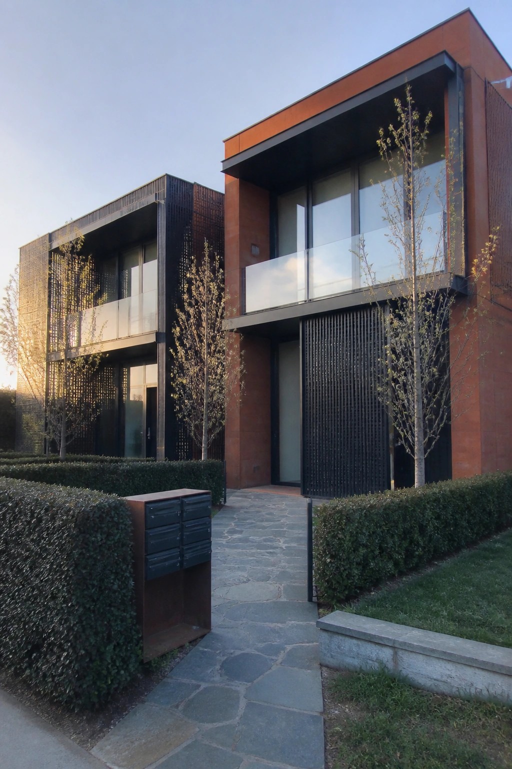Modern townhouses with red-brown facades, black metal panels, glass balconies, and stone path
