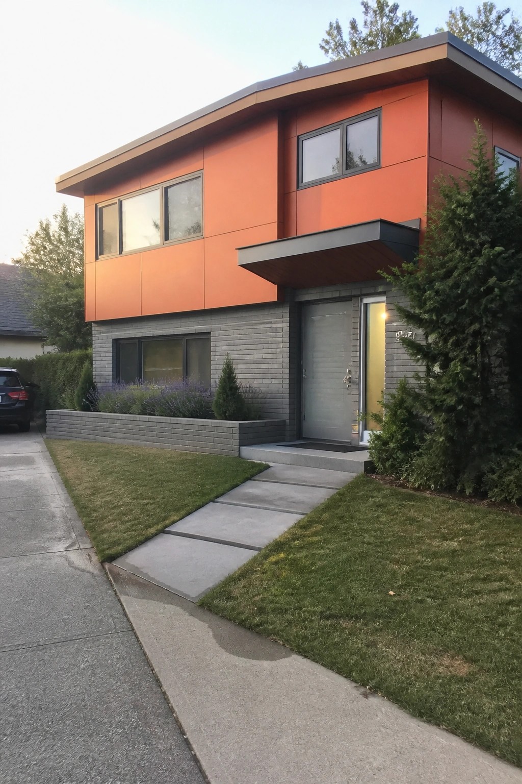 Modern two-story house with orange panels, gray brick base, and concrete path.