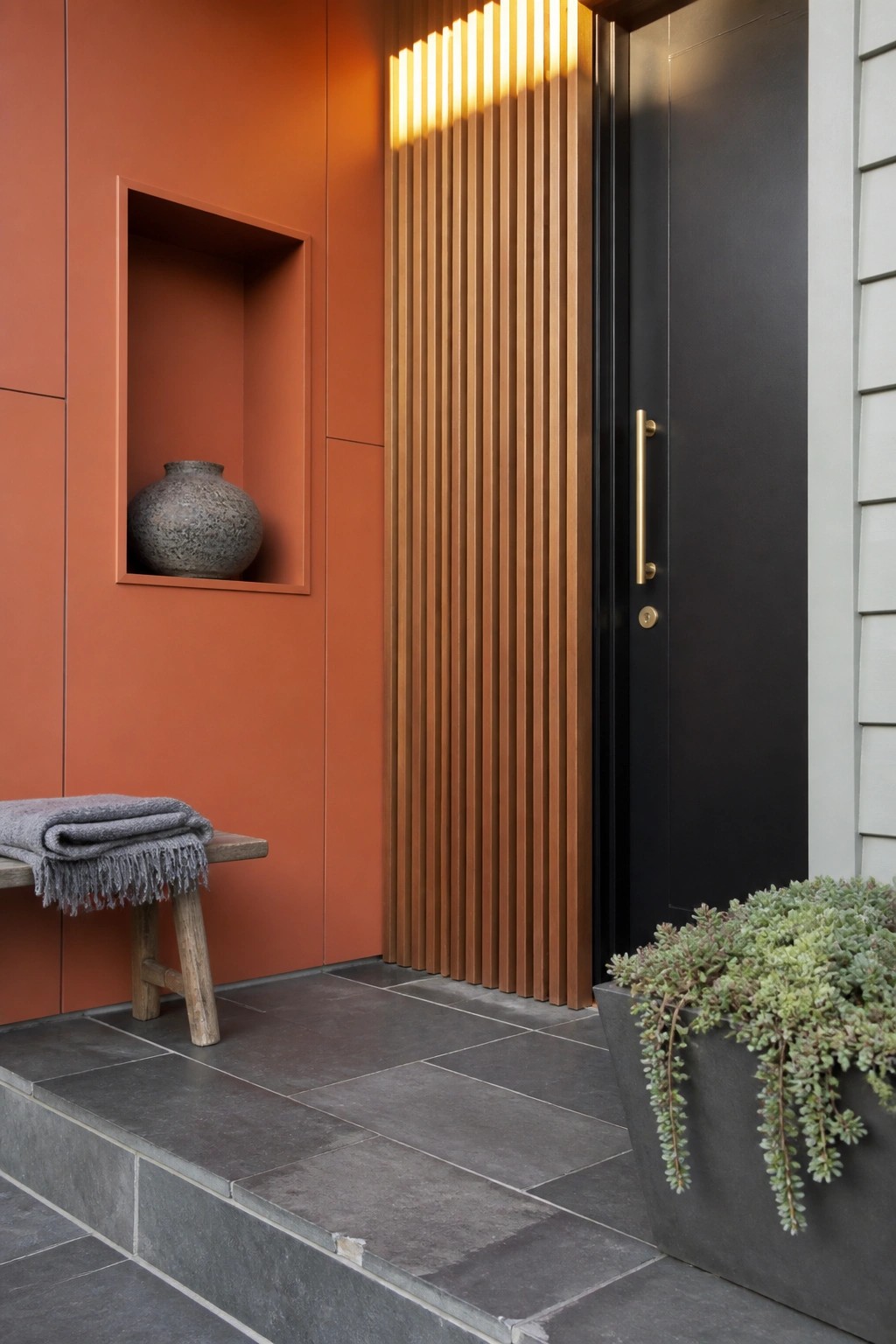 Modern entryway with terracotta wall, black door, wooden bench, and succulent planter.