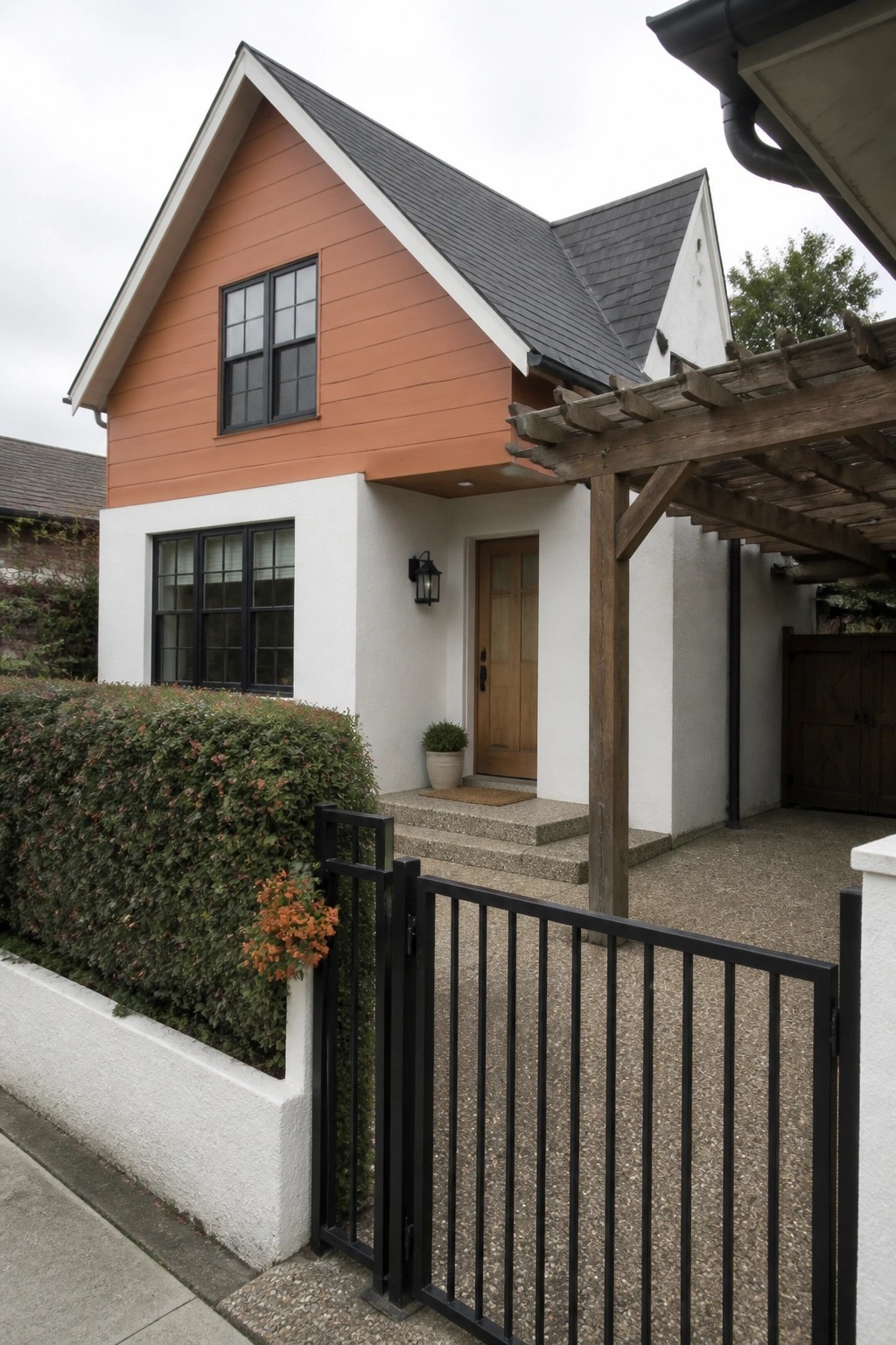 A two-story house exterior with orange fiber cement panels on the upper gable and white stucco on the lower walls, black-framed windows, and a wooden front door.
