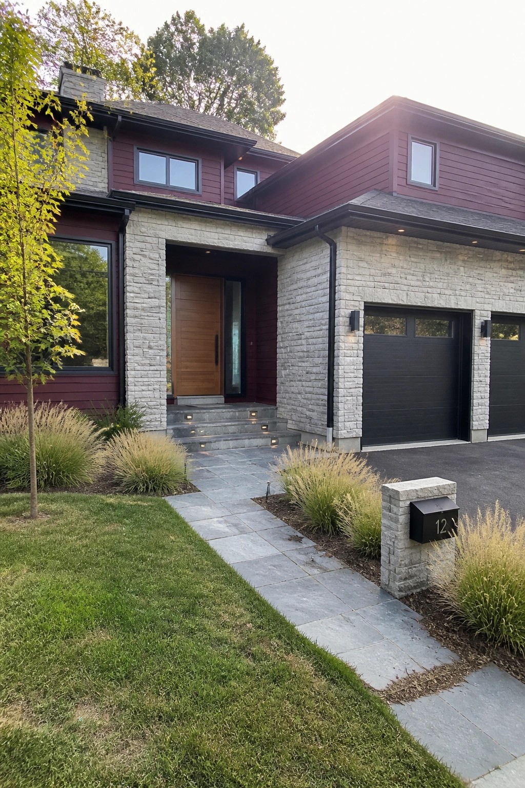 A two-story house with maroon siding, gray stone around the entry and garage, a wooden front door, and two dark garage doors.