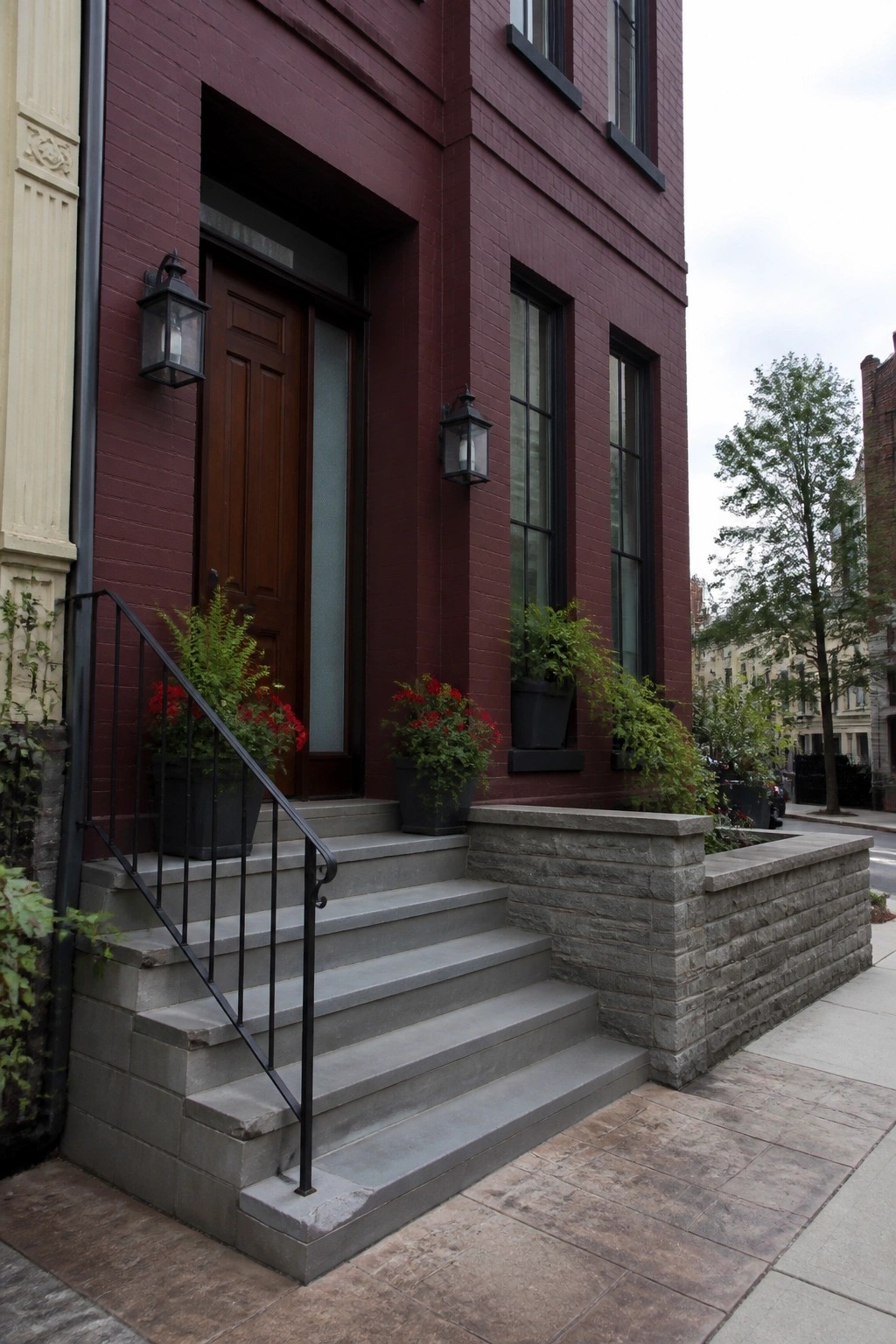 Red brick building entrance with wooden door, gray stairs, and potted plants.