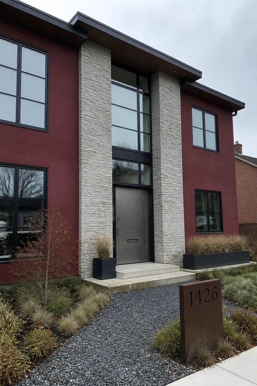 Modern red house with stone pillars, gray door, large windows, and 1426 sign
