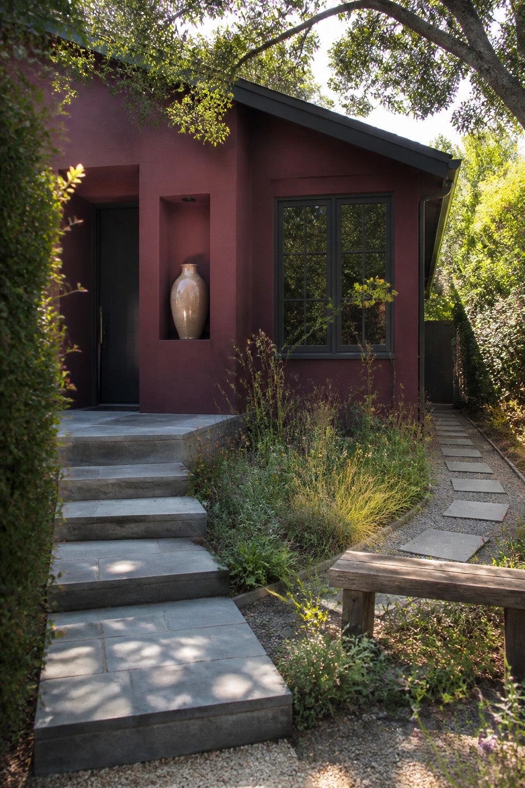 Maroon house with stone steps, vase niche, window, gravel path, and wooden bench