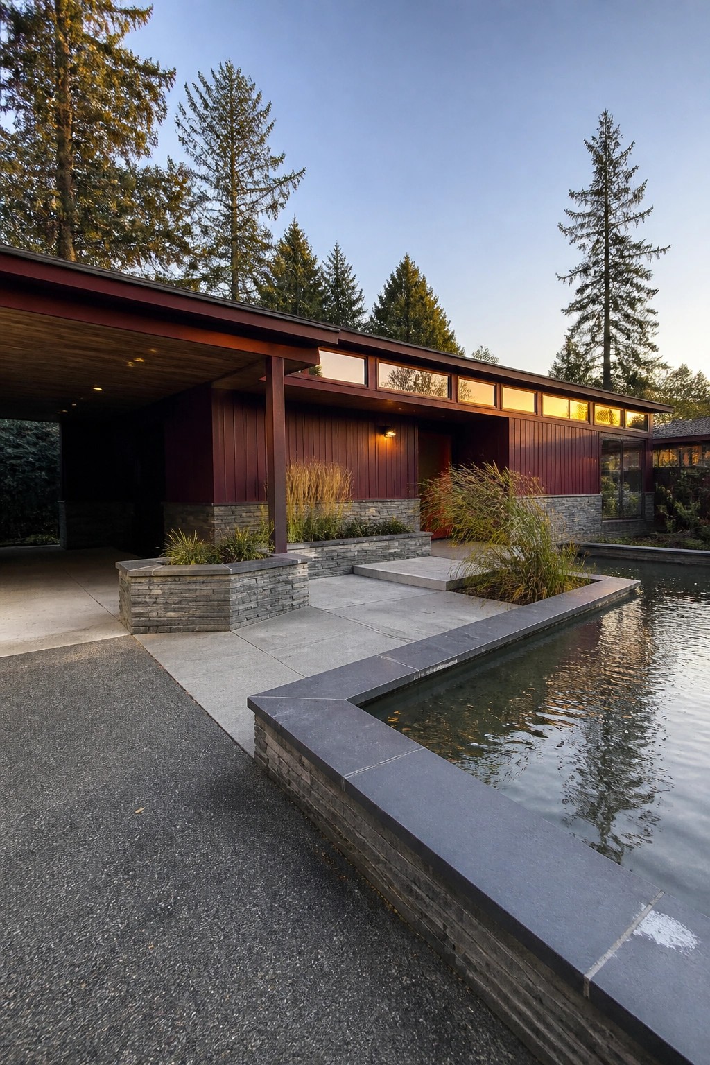 Modern red house with flat roof, stone accents, and reflecting pool amid tall trees