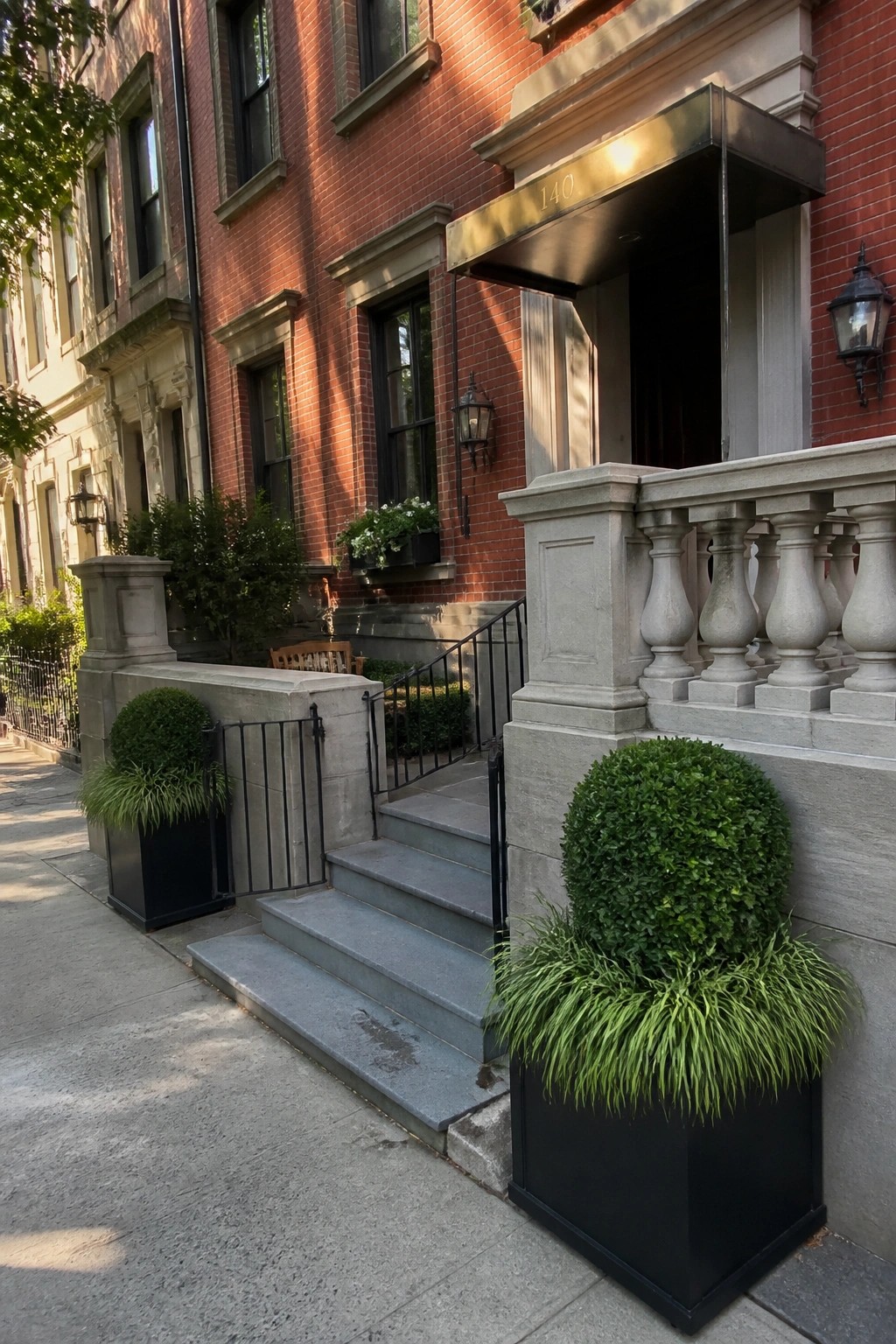 Red brick building entrance with stone stairs, black planters, and metal railings.