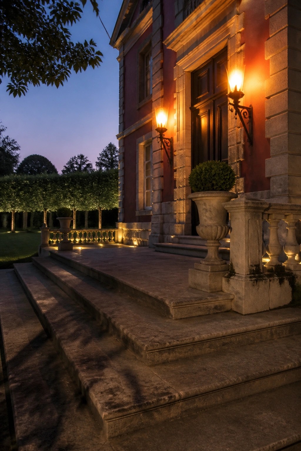 Illuminated stone steps lead to red mansion entrance with glowing lanterns and urn at dusk.