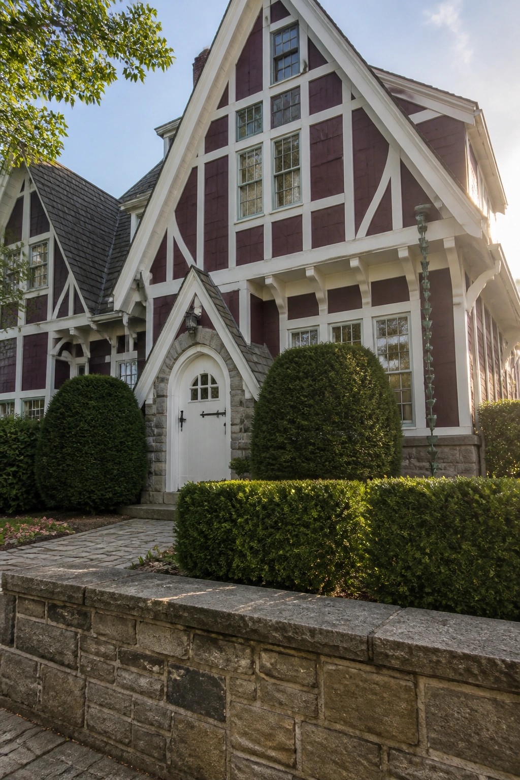 A two-story purple house with white trim outlining steep gables and multiple windows, a white arched door, stone accents, and trimmed green shrubs along the front.