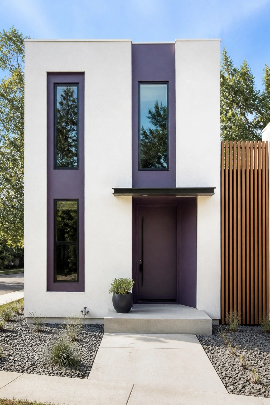 A modern two-story house exterior with white walls, vertical purple panels framing tall windows and the front door, a concrete entry step, and gravel landscaping.