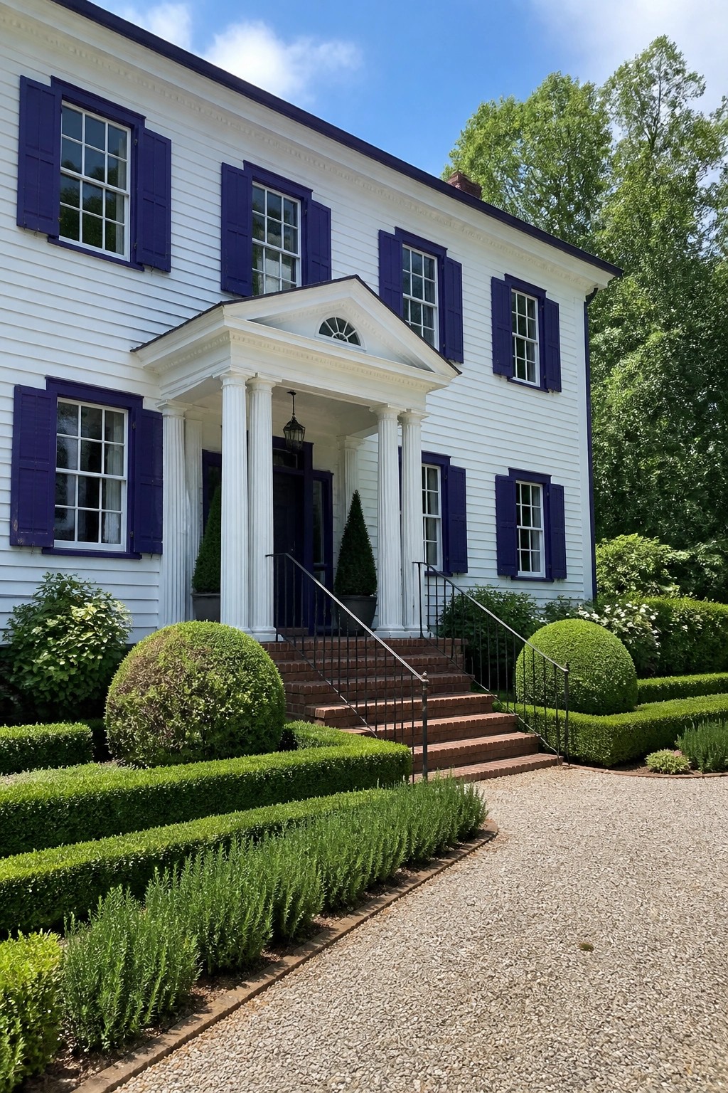 A two-story white house with purple shutters, a white columned portico over the front door, brick steps, and landscaping along a gravel driveway.