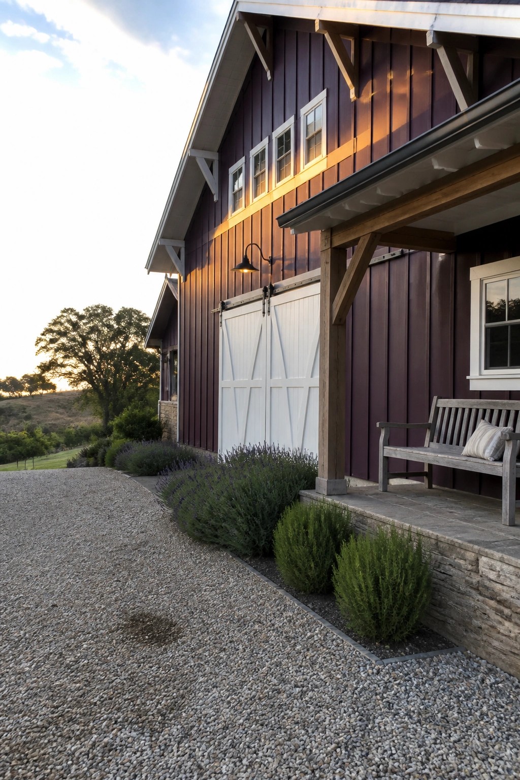 A dark purple barn-style house exterior with white sliding barn doors, white window trim, a stone porch, and a wooden bench beside gravel landscaping.