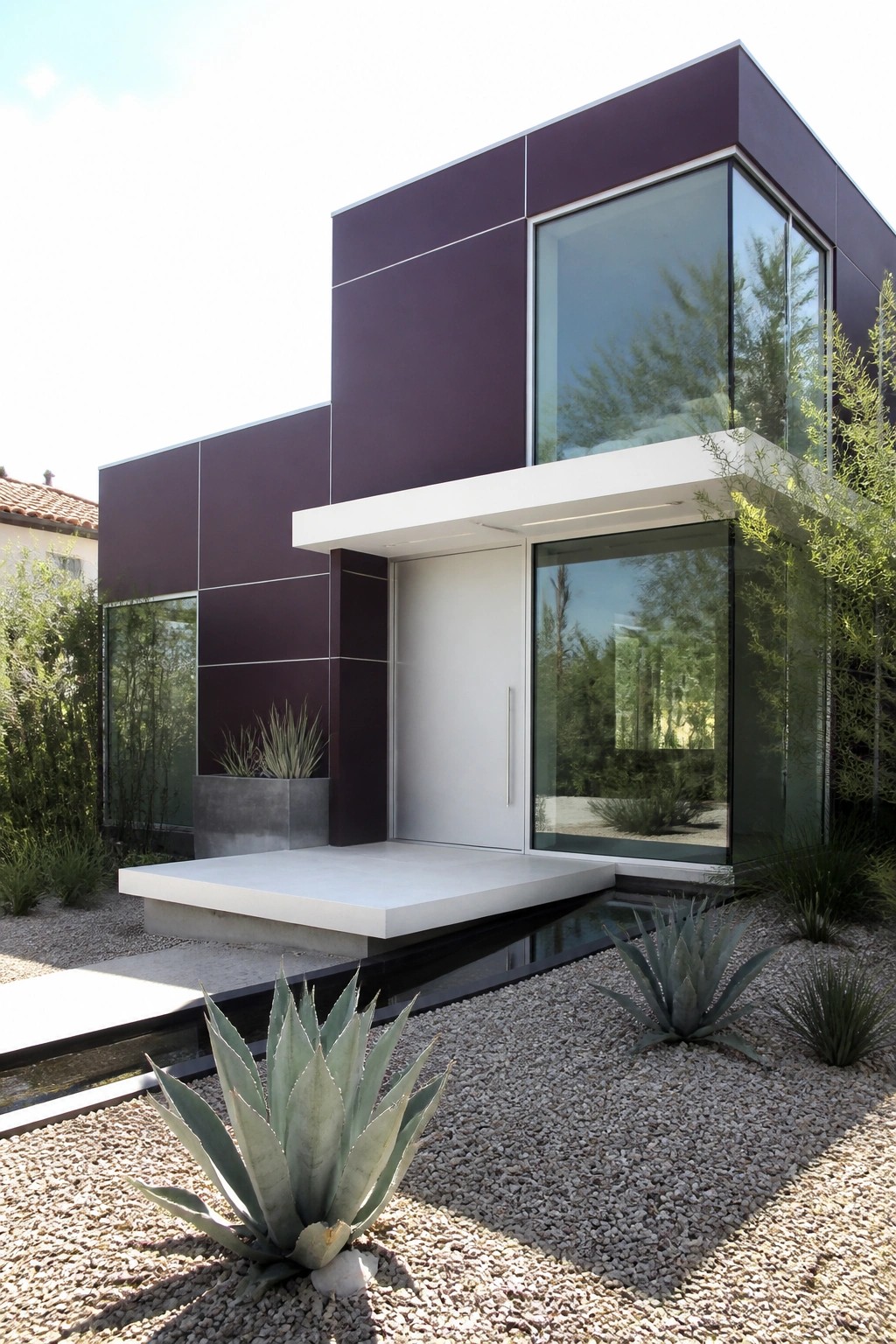 Modern purple house with large glass windows, white door, and agave plants in gravel.