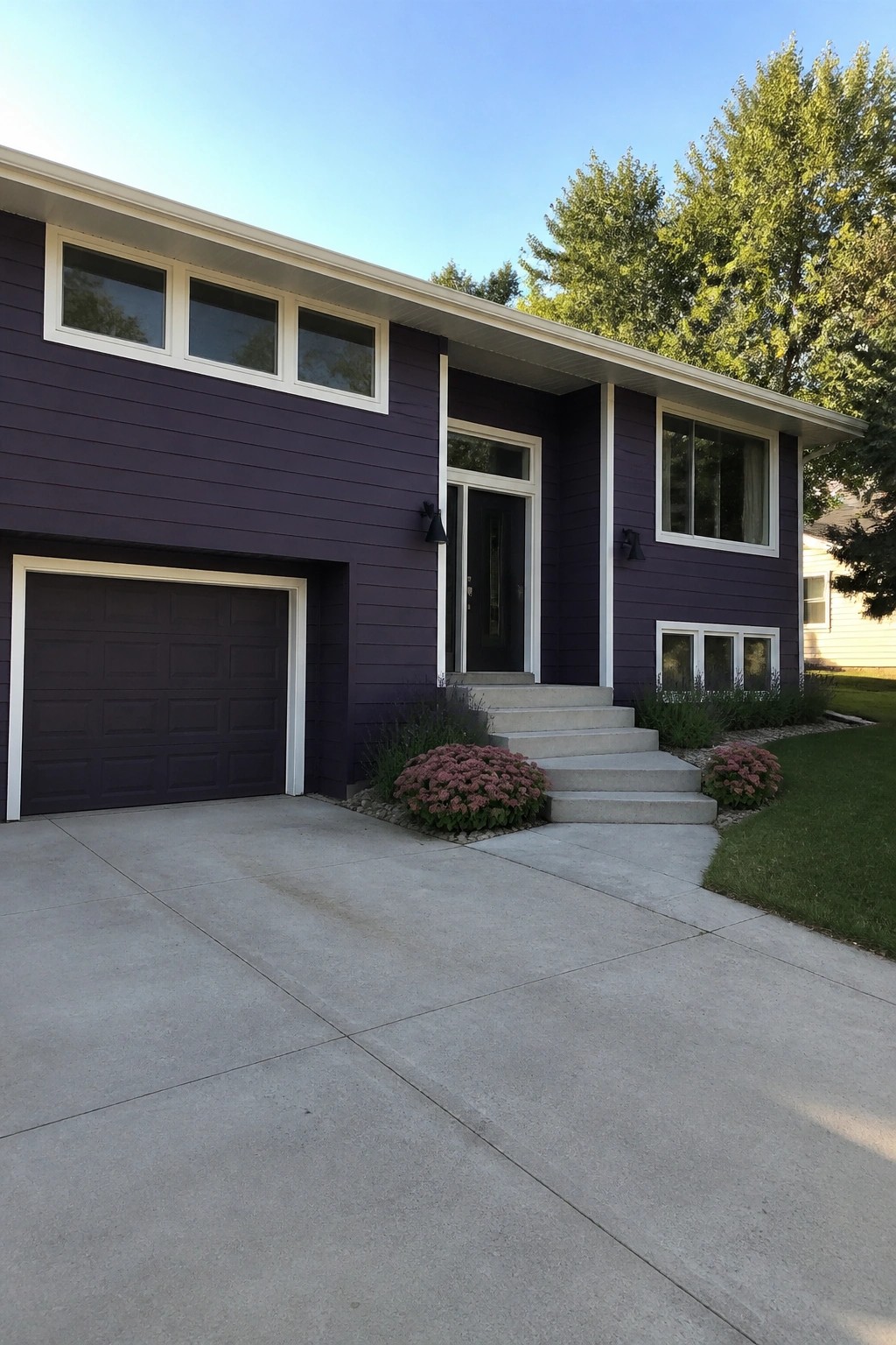 Purple house with white trim, garage, concrete driveway, steps, and pink flowers.