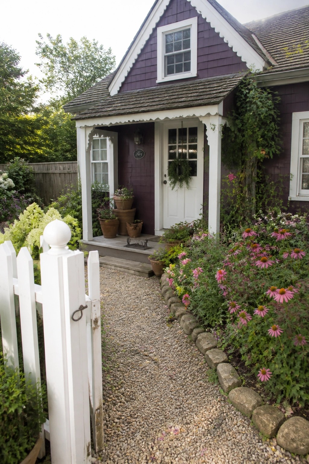 A purple house exterior with white trim, a white front door, and a gravel path bordered by flowers.