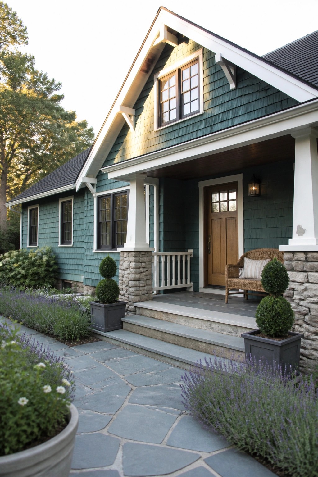 A two-story house with teal cedar shake siding, white trim, a wooden front door, stone porch pillars, and steps leading to a slate path.