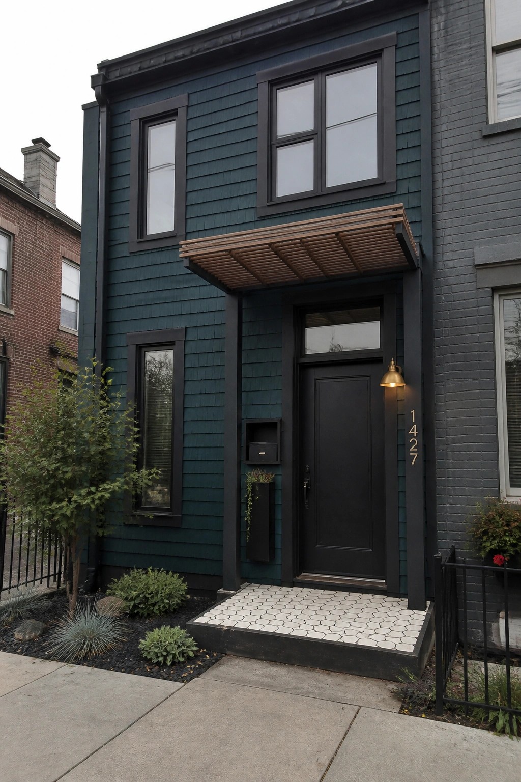 A narrow two-story house with textured teal cedar shake siding, black trim around windows and door, and a small white-tiled entry step.