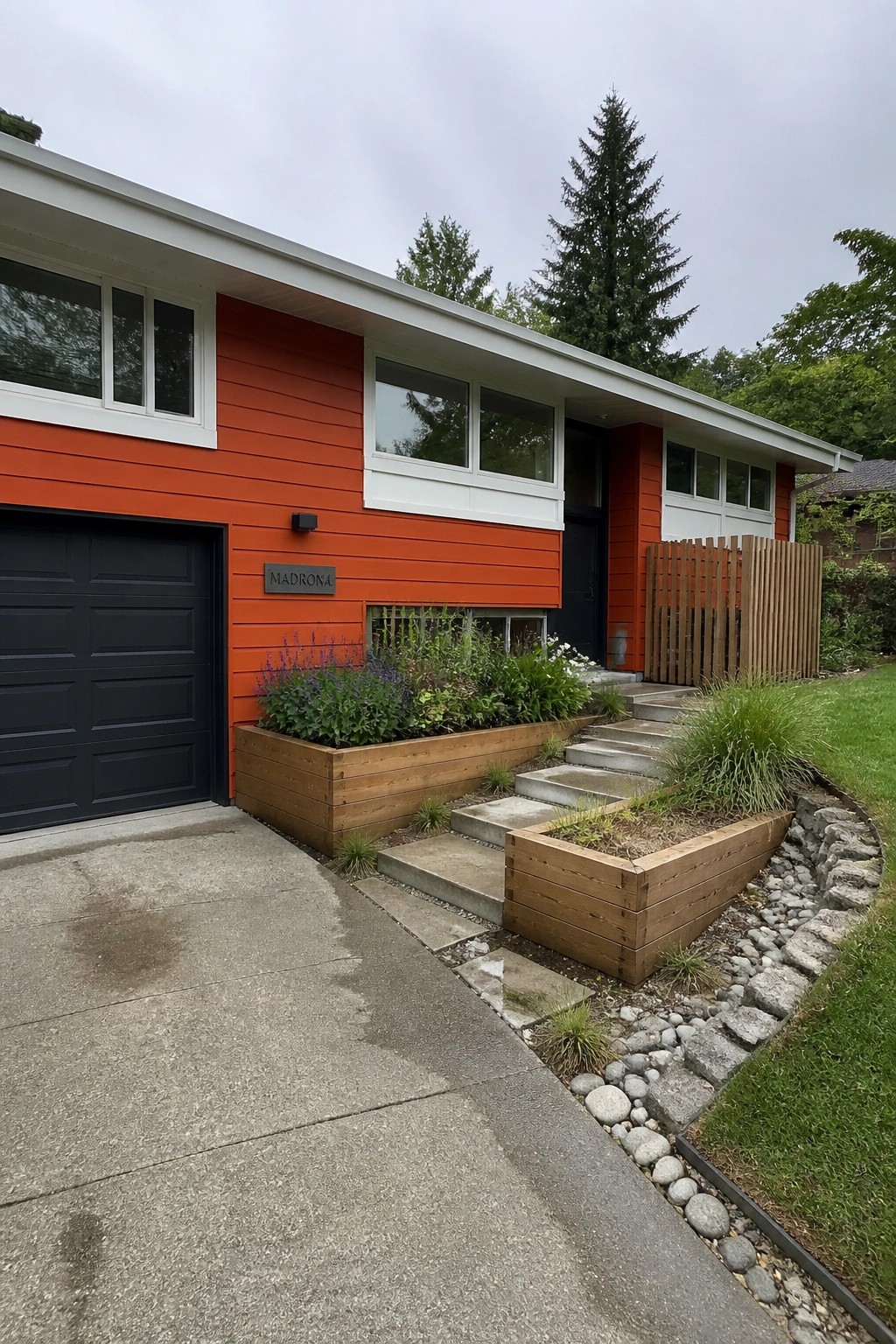 A modern house with bright orange horizontal siding, white trim around the windows and eaves, a black garage door on the left, and concrete steps with wooden planters beside the entrance.