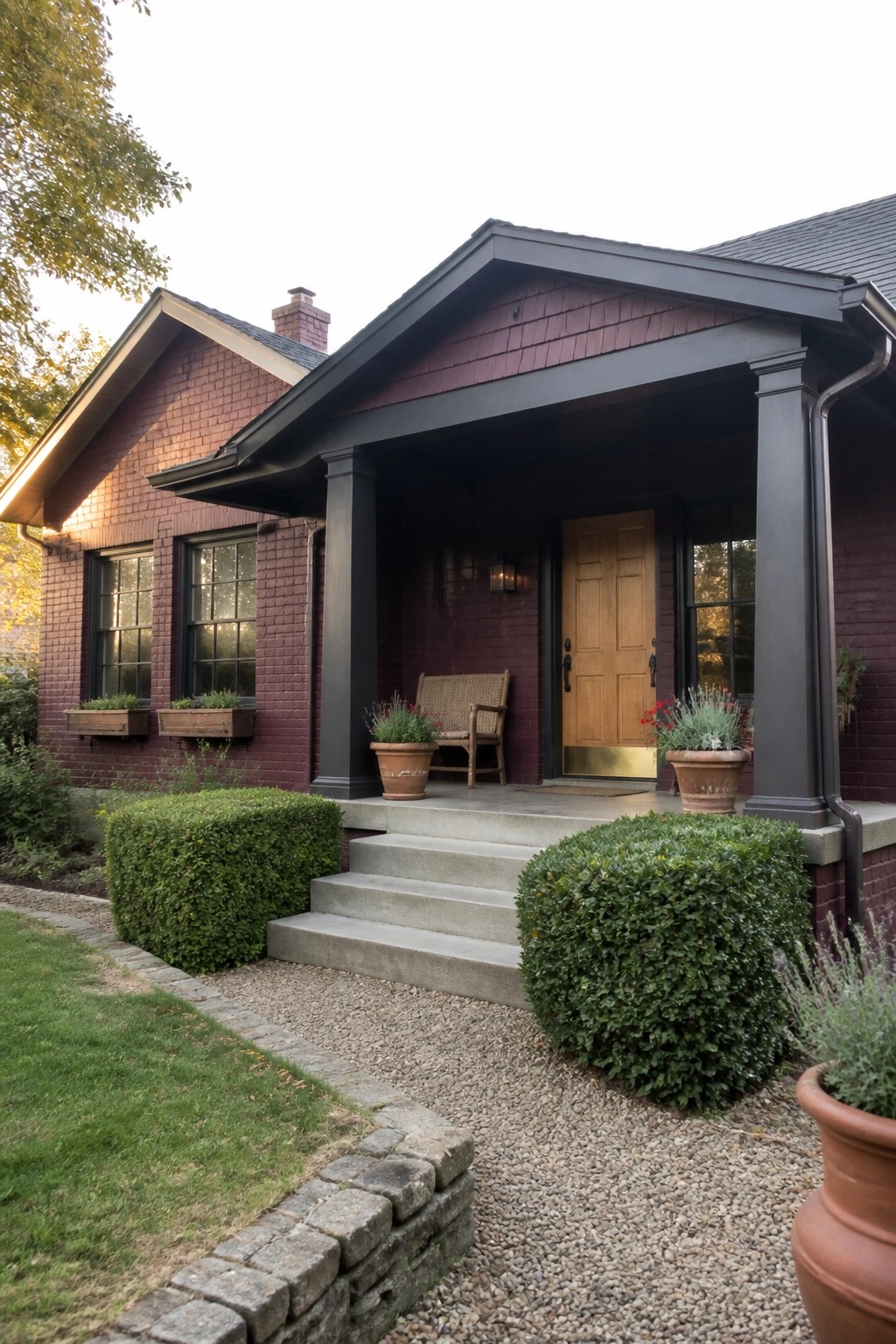 A maroon brick house exterior with dark painted trim, columns, and a gabled porch featuring a wooden front door.