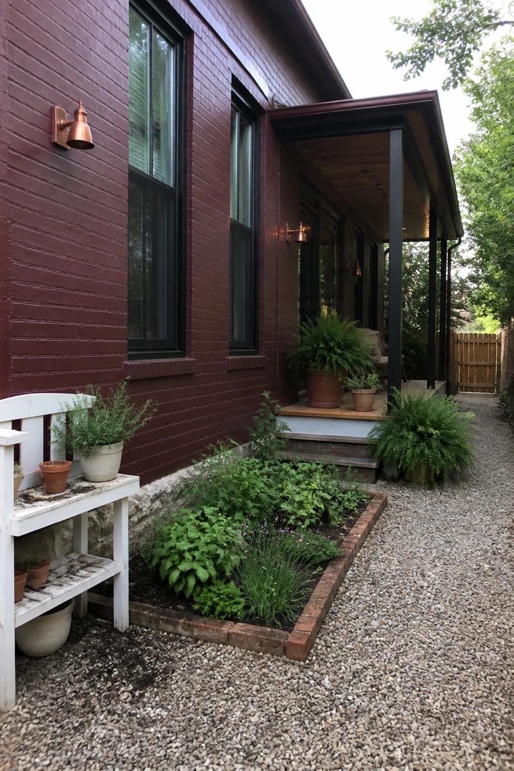 Maroon house with black windows, covered porch, brick garden bed, and gravel path