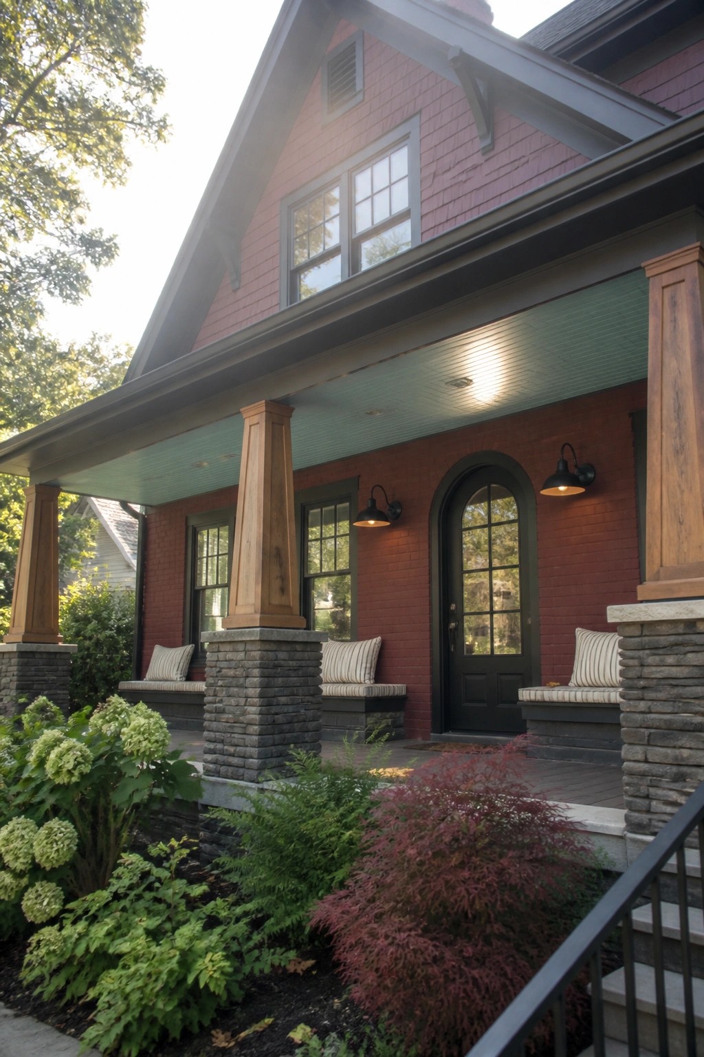 Front view of a maroon brick house with a green painted porch ceiling, wooden columns on stone bases, black arched door, and built-in benches.