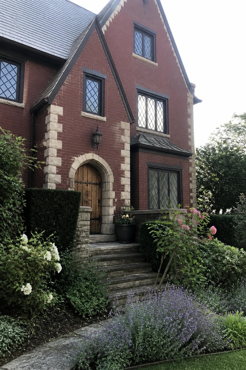 Front view of a two-story maroon brick house with light stone quoins, an arched wooden door, and diamond-paned windows.