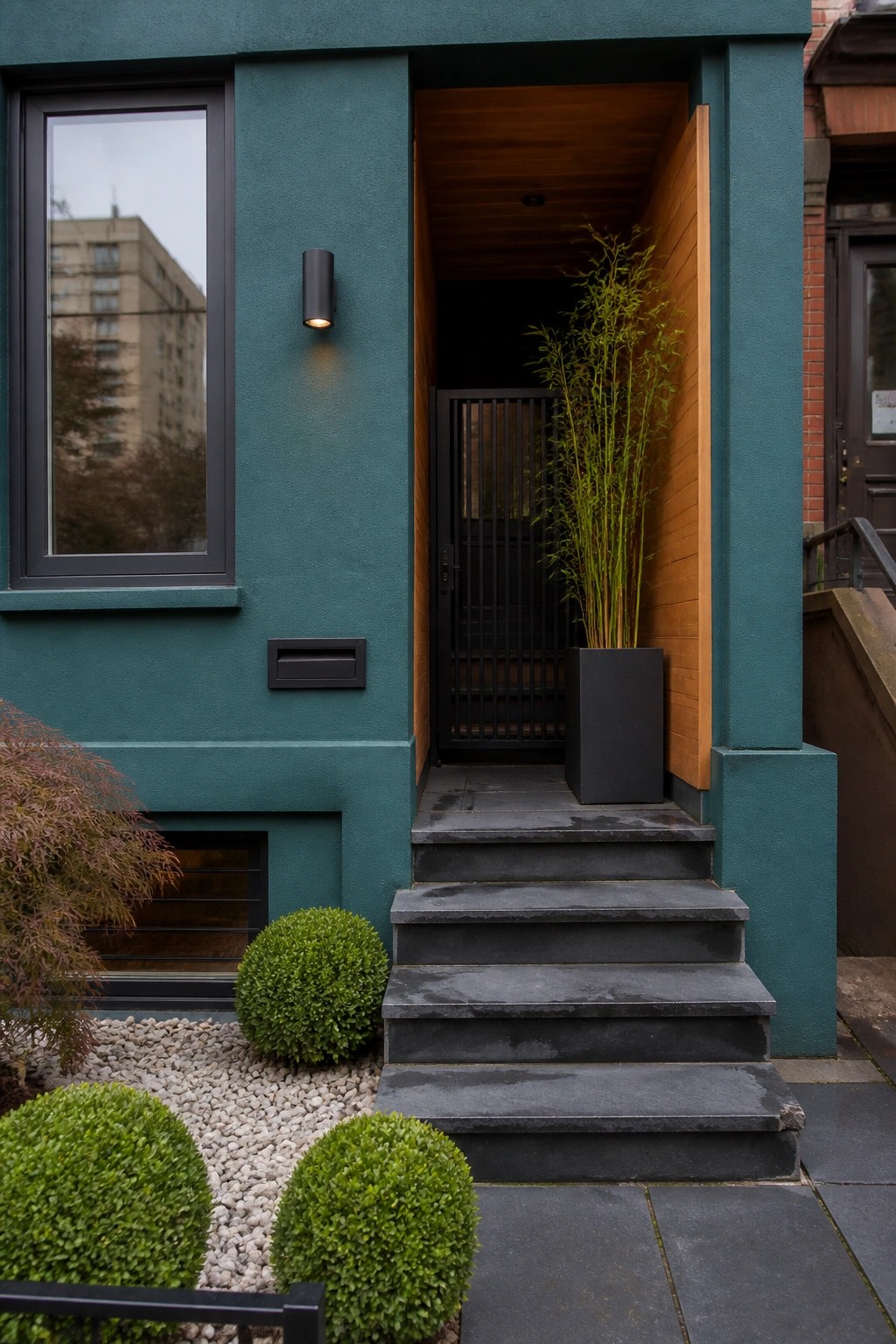 Modern teal house entrance with black stairs, tall plant, and open wooden door.