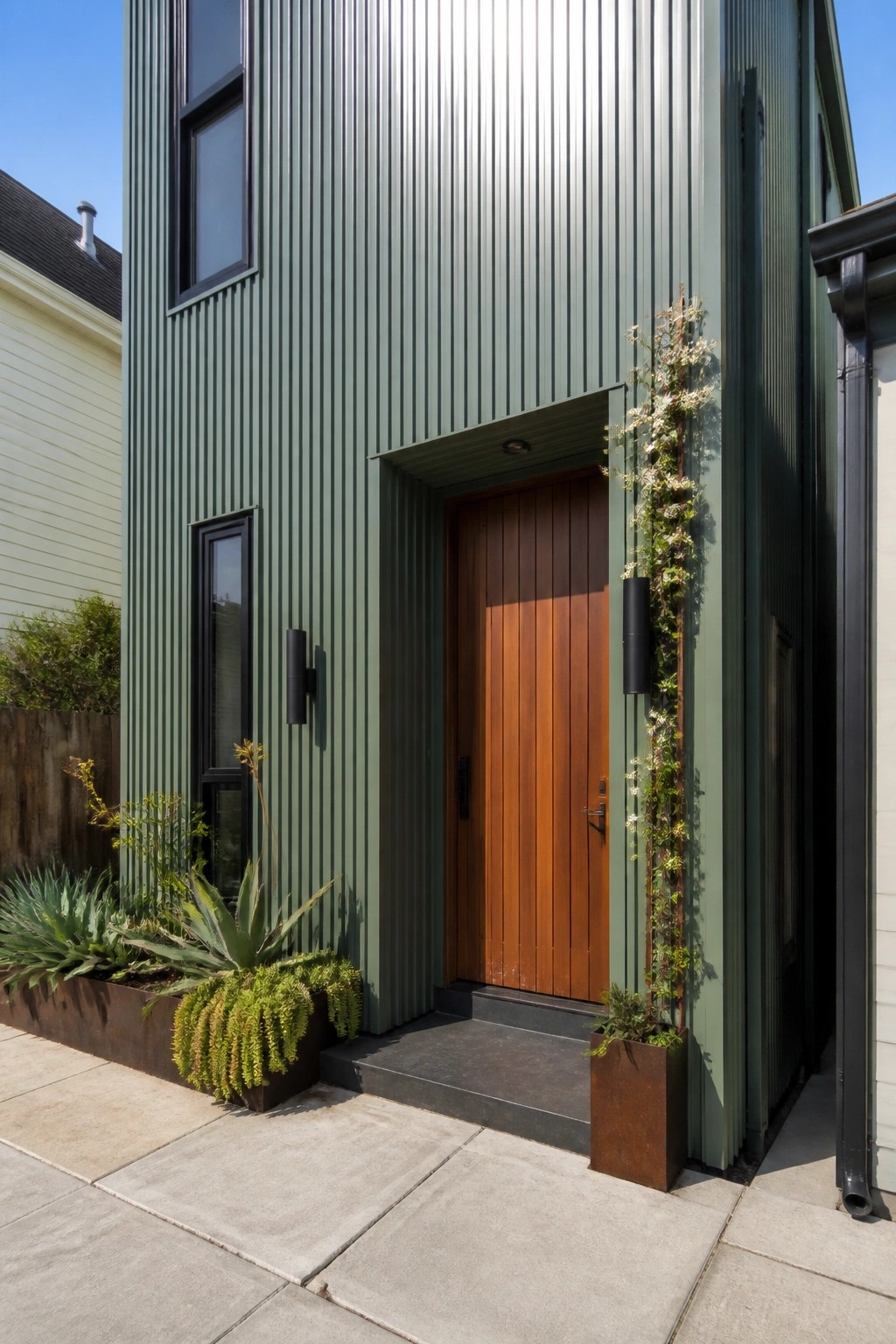 Green corrugated house with wooden door, vertical garden, and metal planters.
