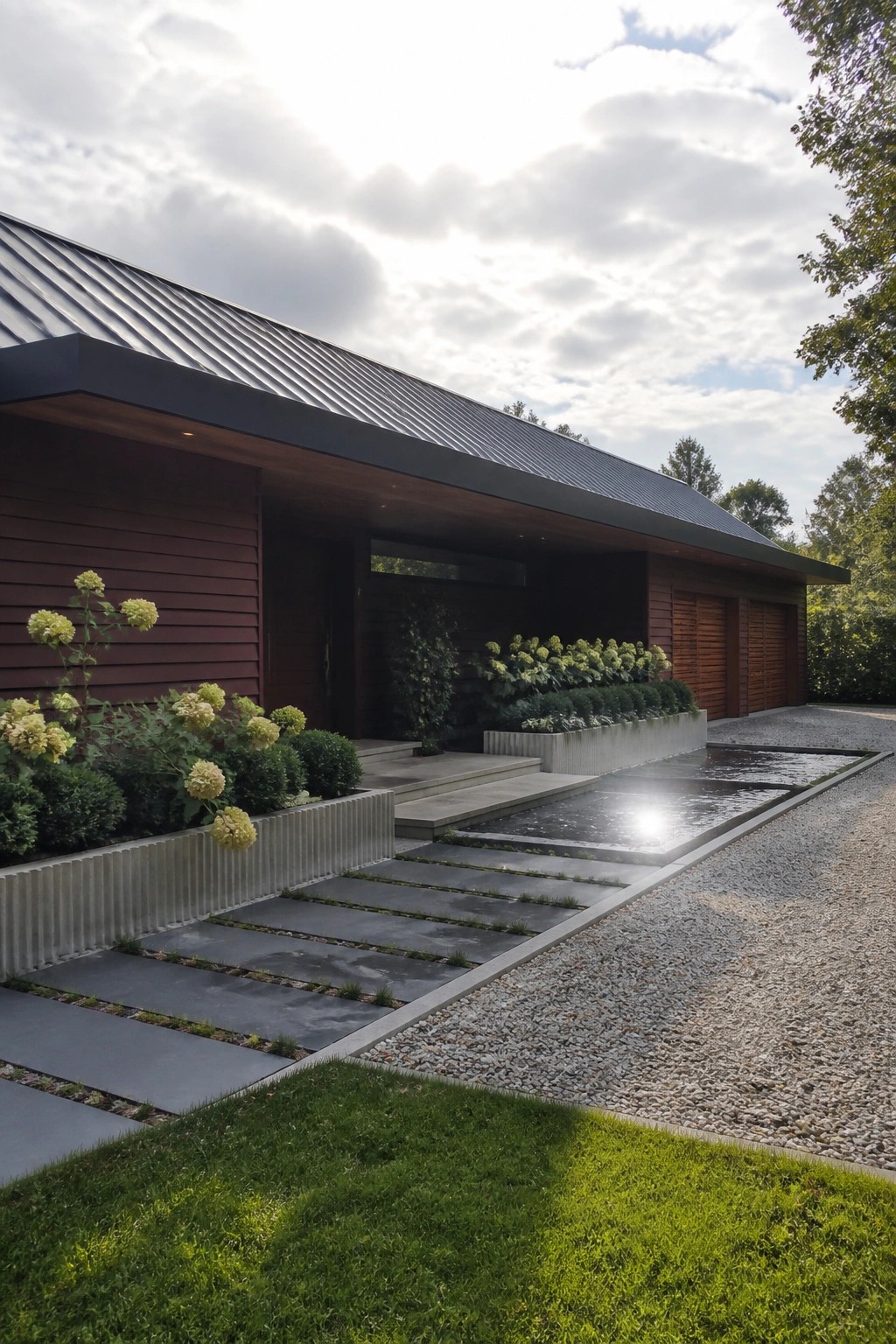 Modern single-story house with dark burgundy horizontal siding, charcoal metal roof, recessed entry, concrete steps, and gravel driveway.