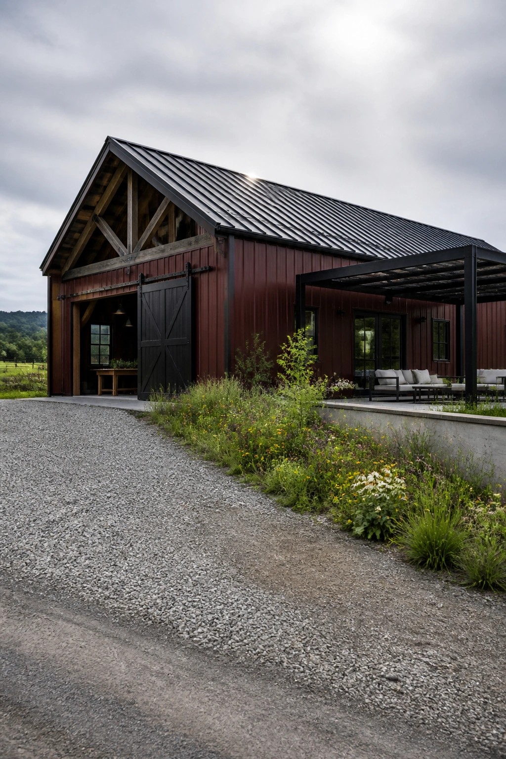 Red barn with open sliding door, black roof, pergola, and wildflower-lined gravel path