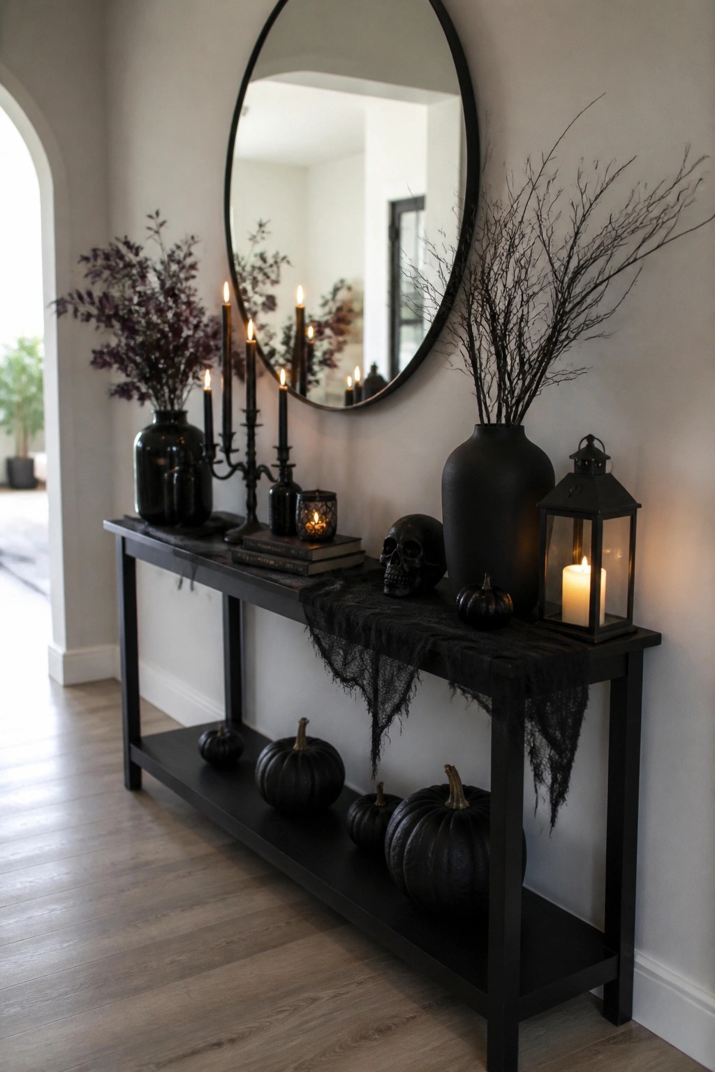Black console table in an entryway styled with a human skull, black candles in candelabras, dark branches, and black gauze.