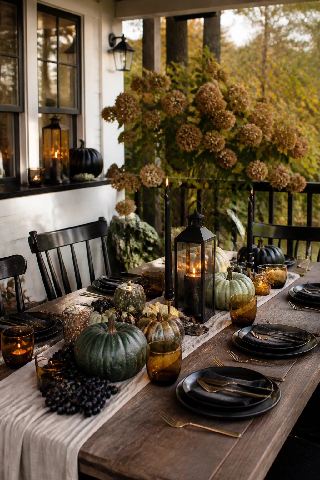 Outdoor wooden dining table styled with black candles, black lanterns, dark pumpkins, and amber glassware arranged along a linen runner.