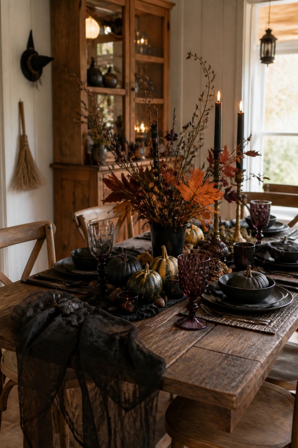 Farmhouse dining table set with black pumpkins, dark candles, purple glassware, and a large branch centerpiece.