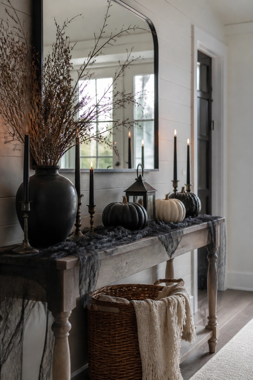 Rustic console table with lit black candles, pumpkins, dried branches, and mirror above.
