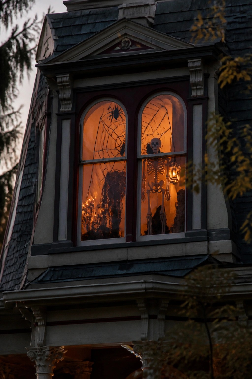 Upper house window showing a skeleton behind the glass with large spiderwebs and a hanging lantern.