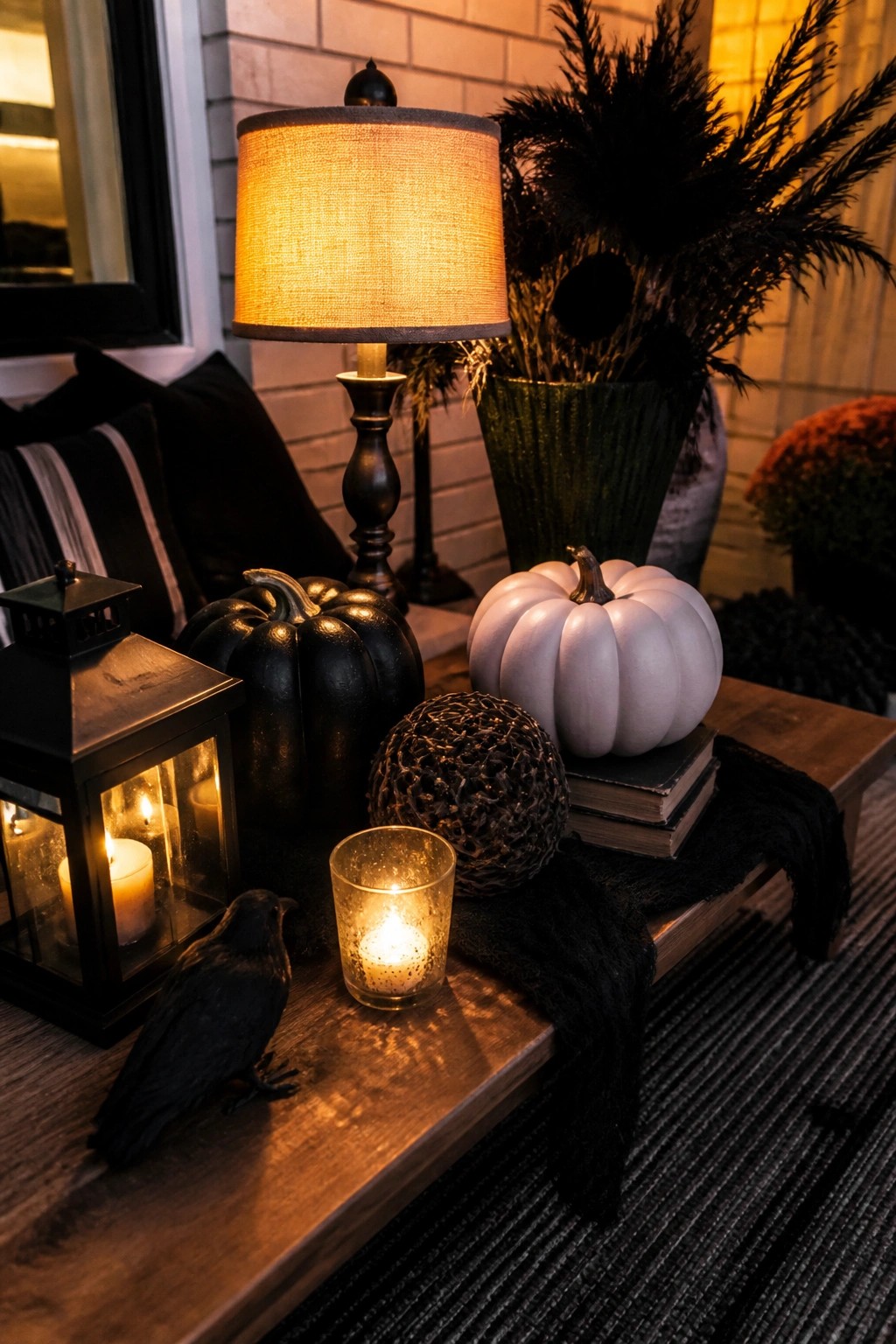 Autumn porch table with black and white pumpkins, lit lantern, candles, and crow figurine