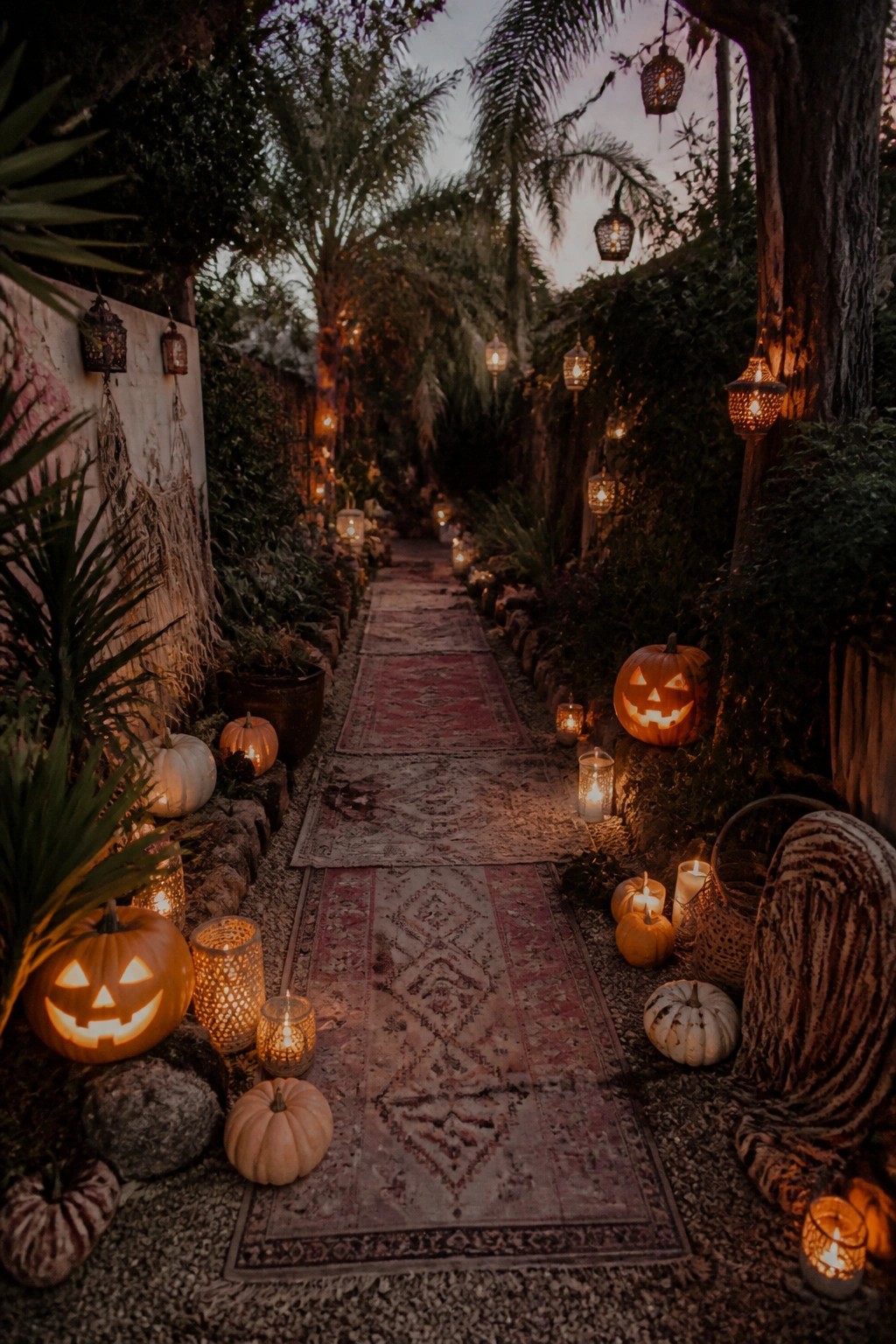 Glowing jack-o'-lanterns and candles line a rug-covered garden path at dusk.